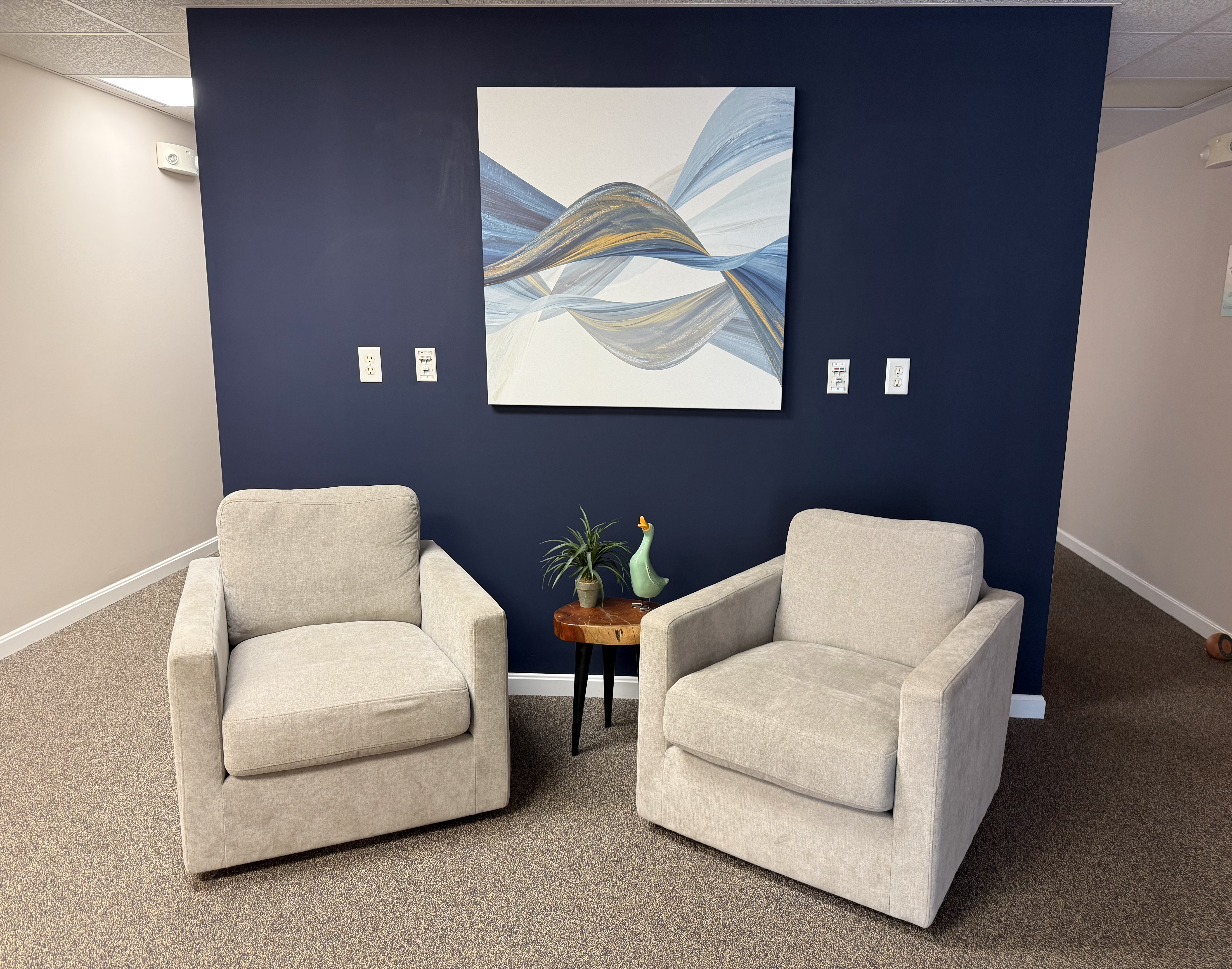 Dr. Monica Hurt's therapy room — two cream chairs facing each other before a navy accent wall with abstract blue and gold artwork